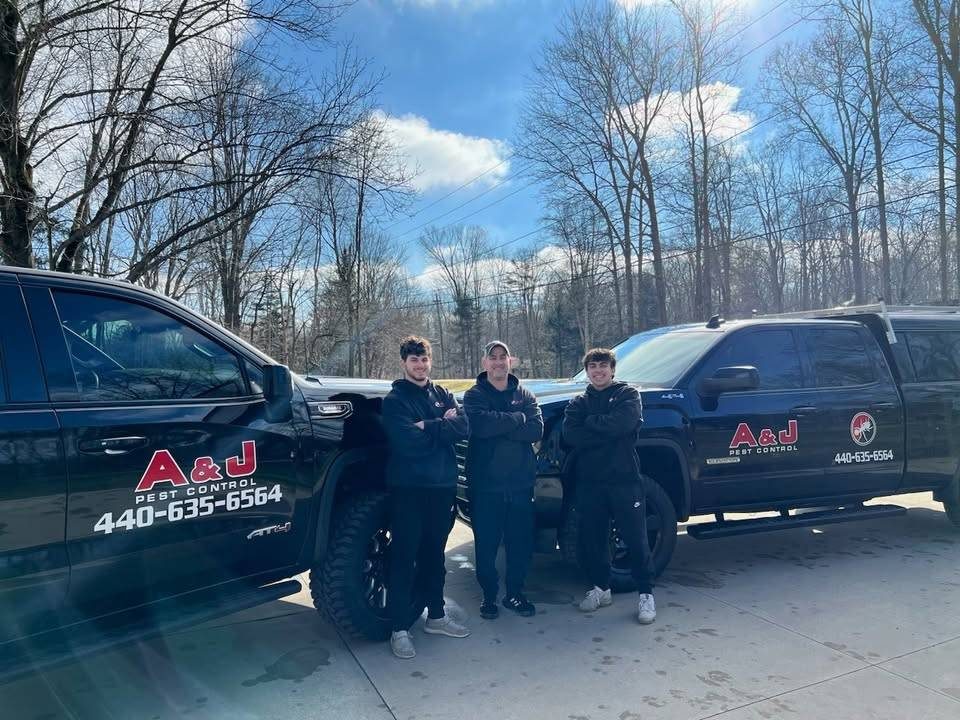 The A&J Pest Control family team standing between two company trucks